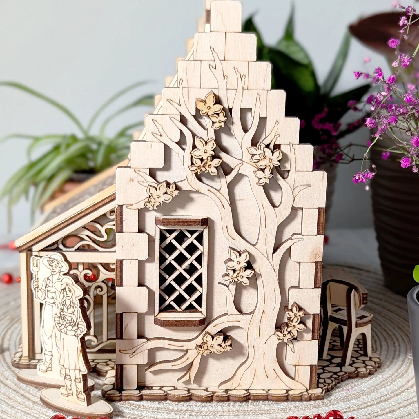 A side angle shot of a laser cut plywood garden cottage showcasing a large intricately engraved blooming tree on the wall.