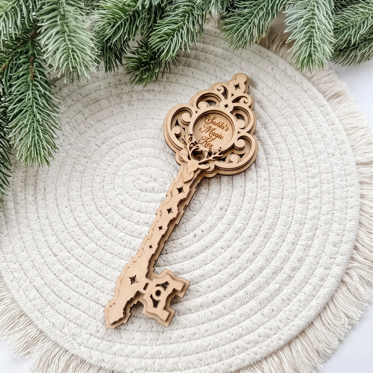 Layered laser cut plywood Santa magic key ornament placed on round woven placemat beside natural evergreen pine branches.
