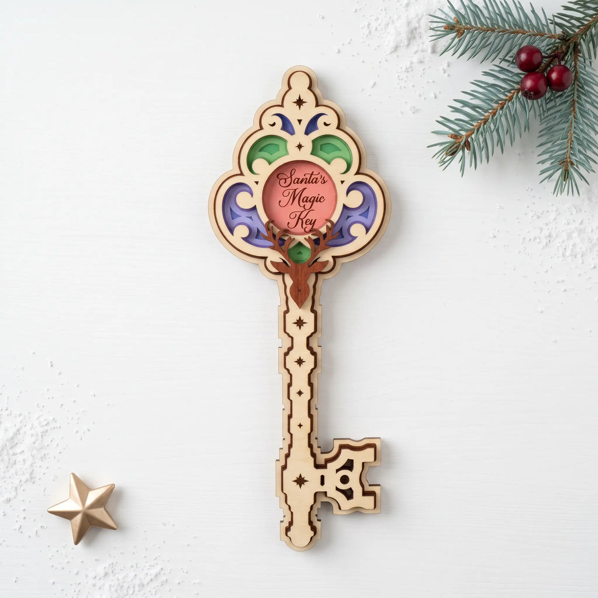 Colorful layered laser cut plywood Santa magic key ornament with deer head on white table with pine branch and gold star.