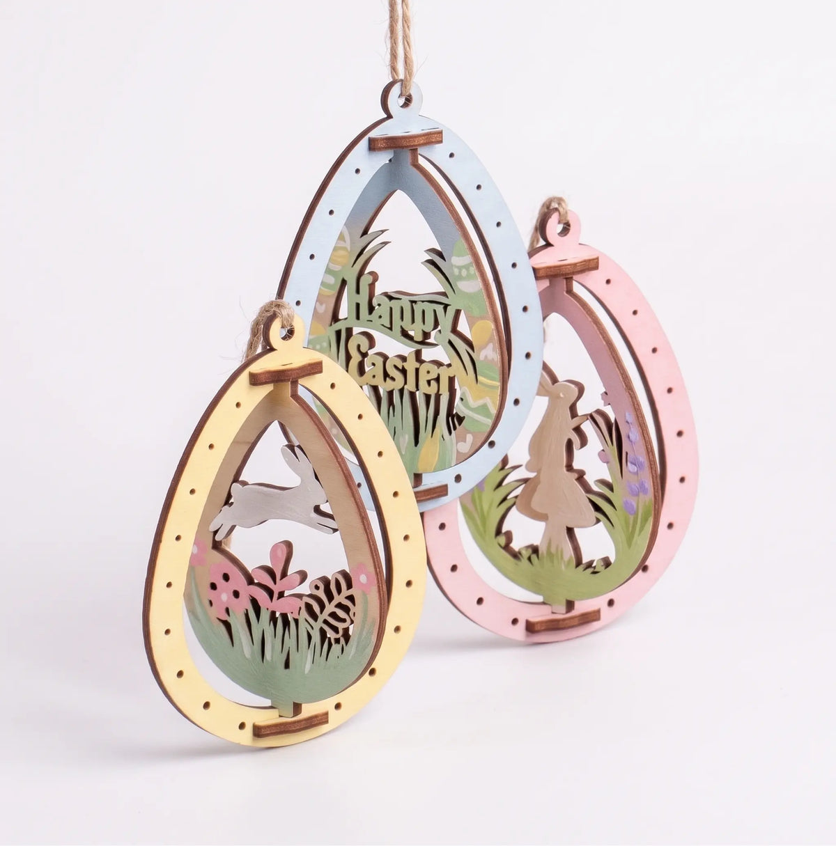 Set of 3 painted laser cut plywood Easter egg ornaments with cute rotating bunnies and holiday lettering on twine strings.