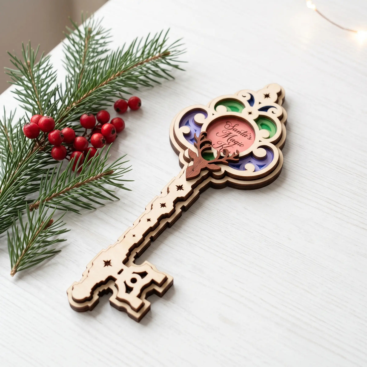 Multicolor laser cut plywood Santa magic key ornament lying on white wooden tabletop next to fresh pine and red berries.