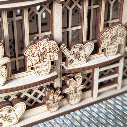 Macro shot of engraved plants and watering cans on a miniature greenhouse wall made of layered laser cut plywood.