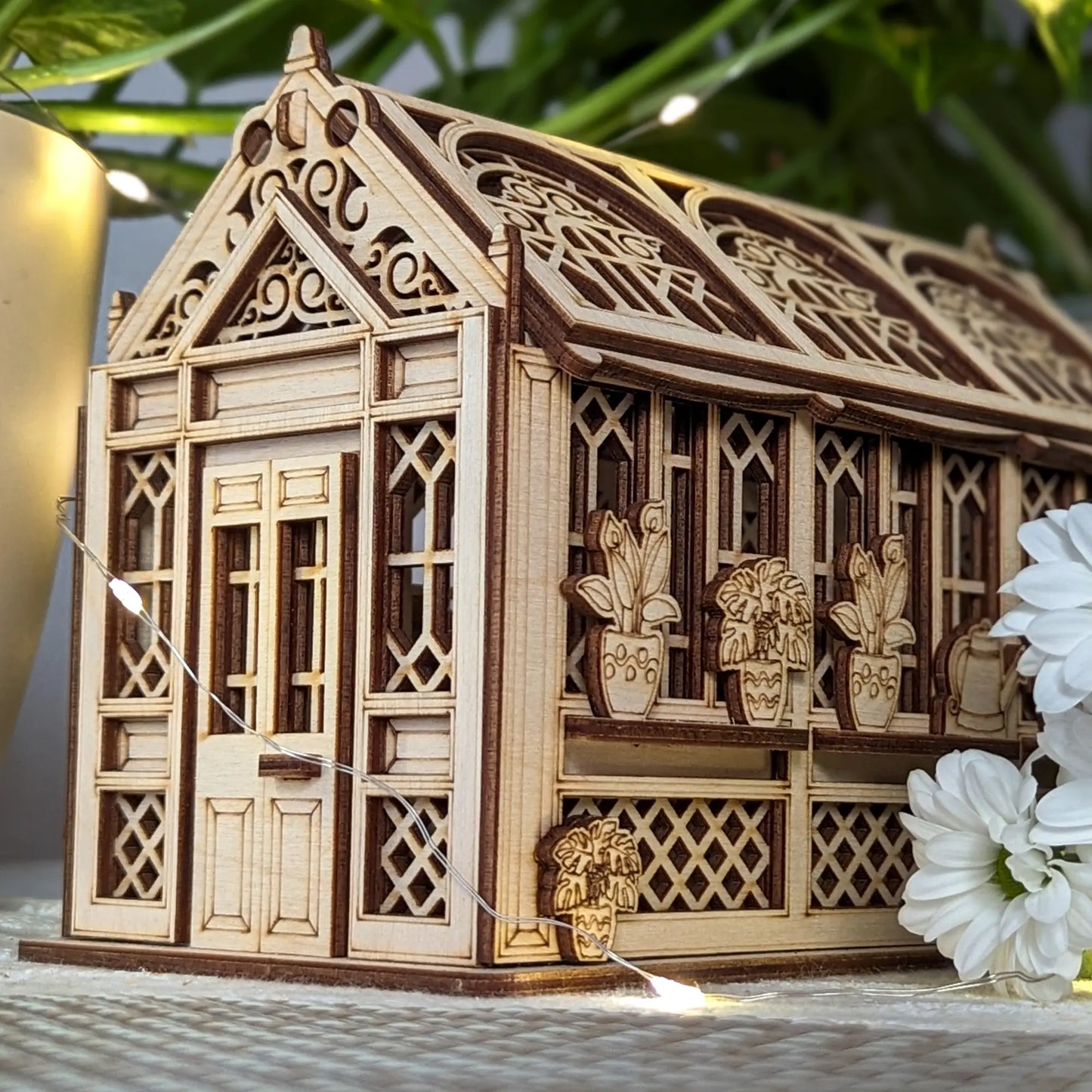 Front facade of a vintage style laser cut plywood greenhouse casket with warm fairy lights and white chrysanthemums.