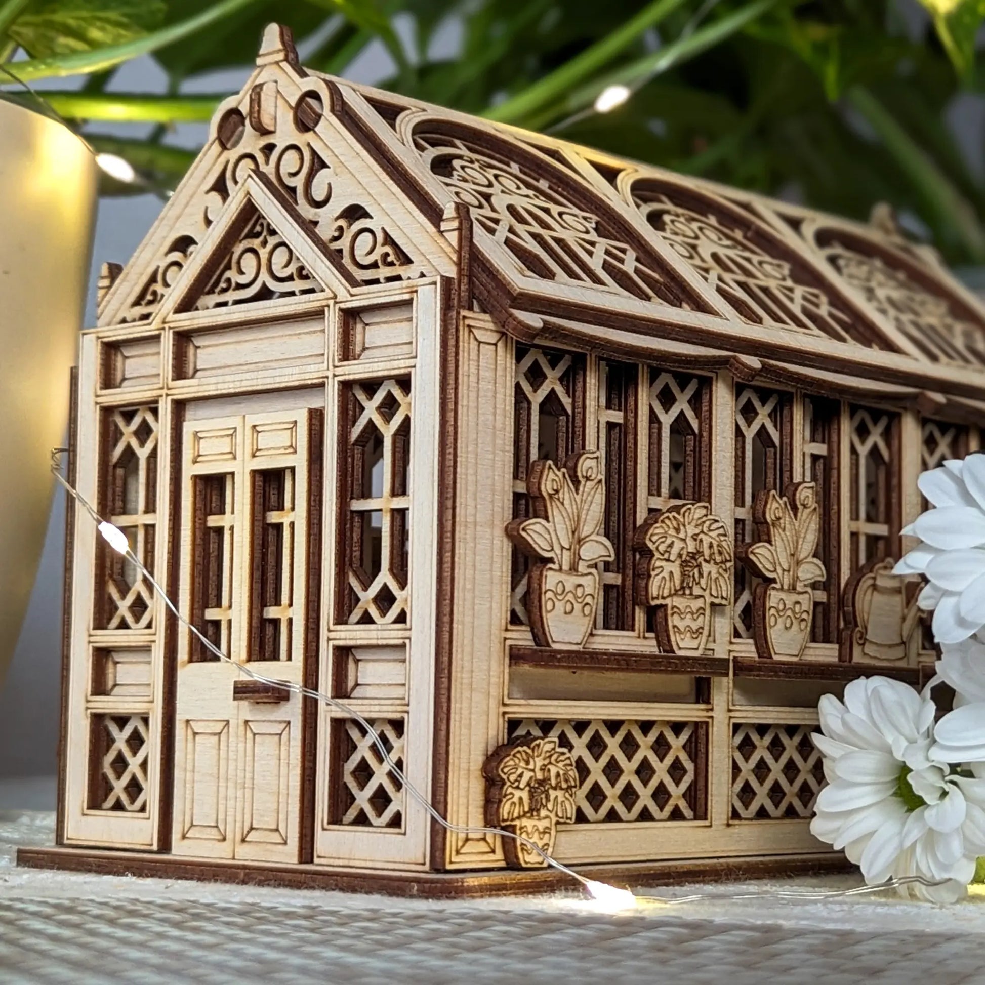 Front facade of a vintage style laser cut plywood greenhouse casket with warm fairy lights and white chrysanthemums.