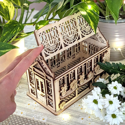 Hand opening the decorated roof of a laser cut plywood greenhouse jewelry box, showcasing its scale and functionality.