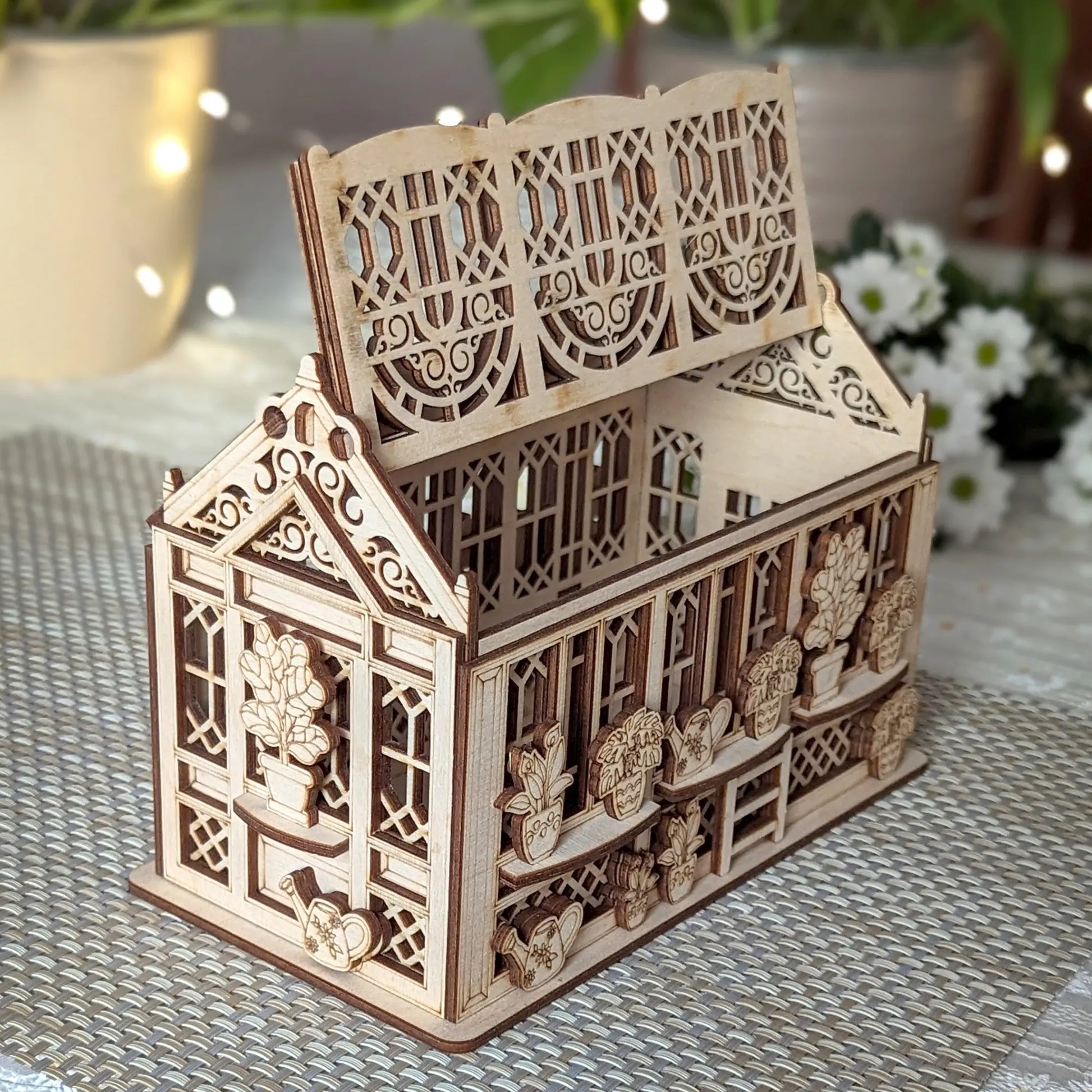 Open laser cut plywood greenhouse box with hinged roof lifted, showing hollow interior and detailed plant engravings.