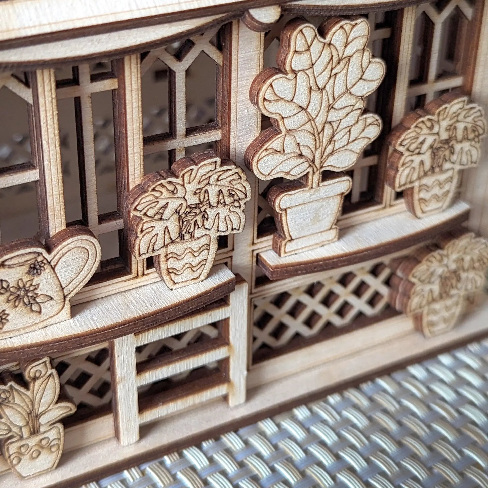 Detailed view of laser cut plywood greenhouse wall with engraved potted plants on small shelves and lattice patterns.