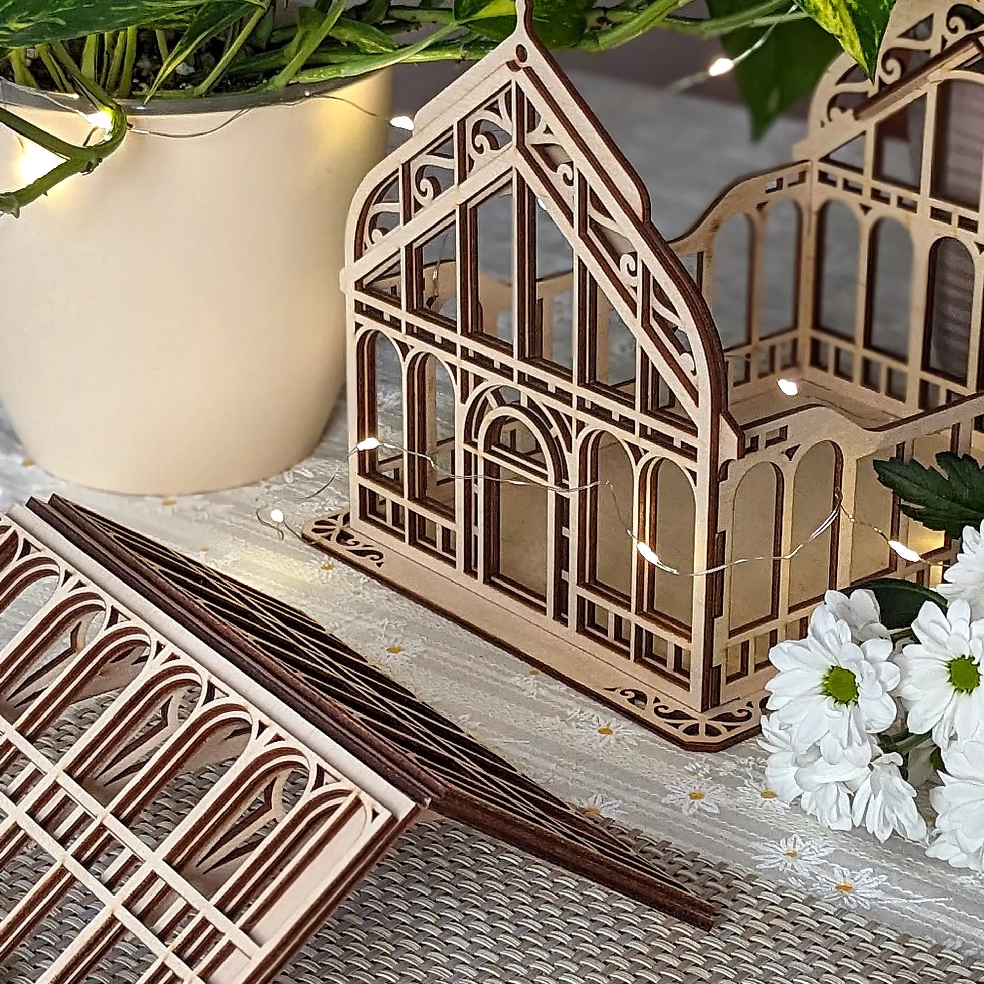 Close-up view of an open laser cut plywood miniature greenhouse frame with intricate carved window patterns.