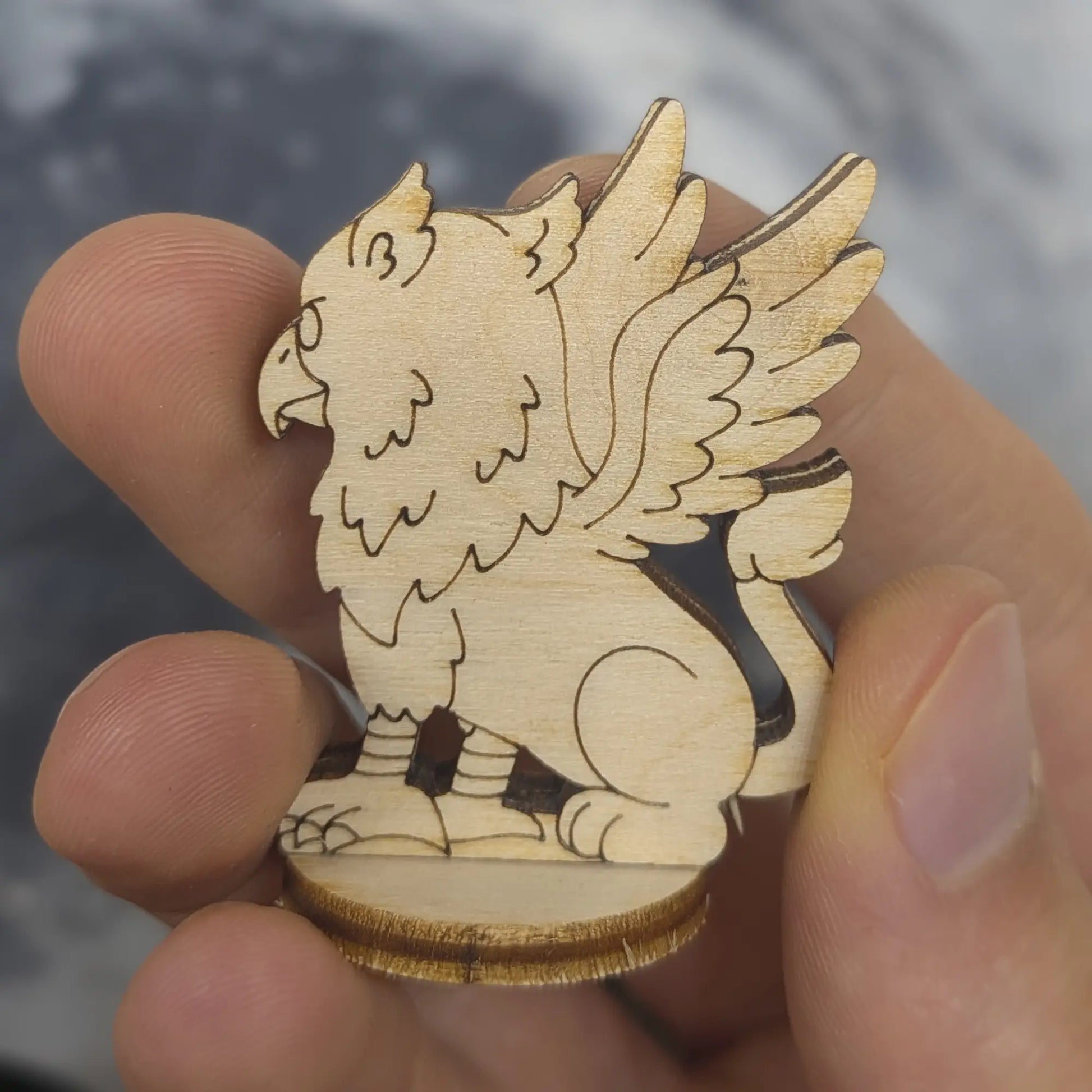 Back view of a laser cut plywood griffin held in hand. Highlights the dark burnt edges and intricate tail and wing carvings