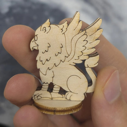 Back view of a laser cut plywood griffin held in hand. Highlights the dark burnt edges and intricate tail and wing carvings