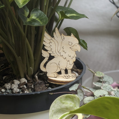 Laser cut plywood griffin figurine sits in a plant pot. Features eagle wings, lion body, and fine engraved feather details