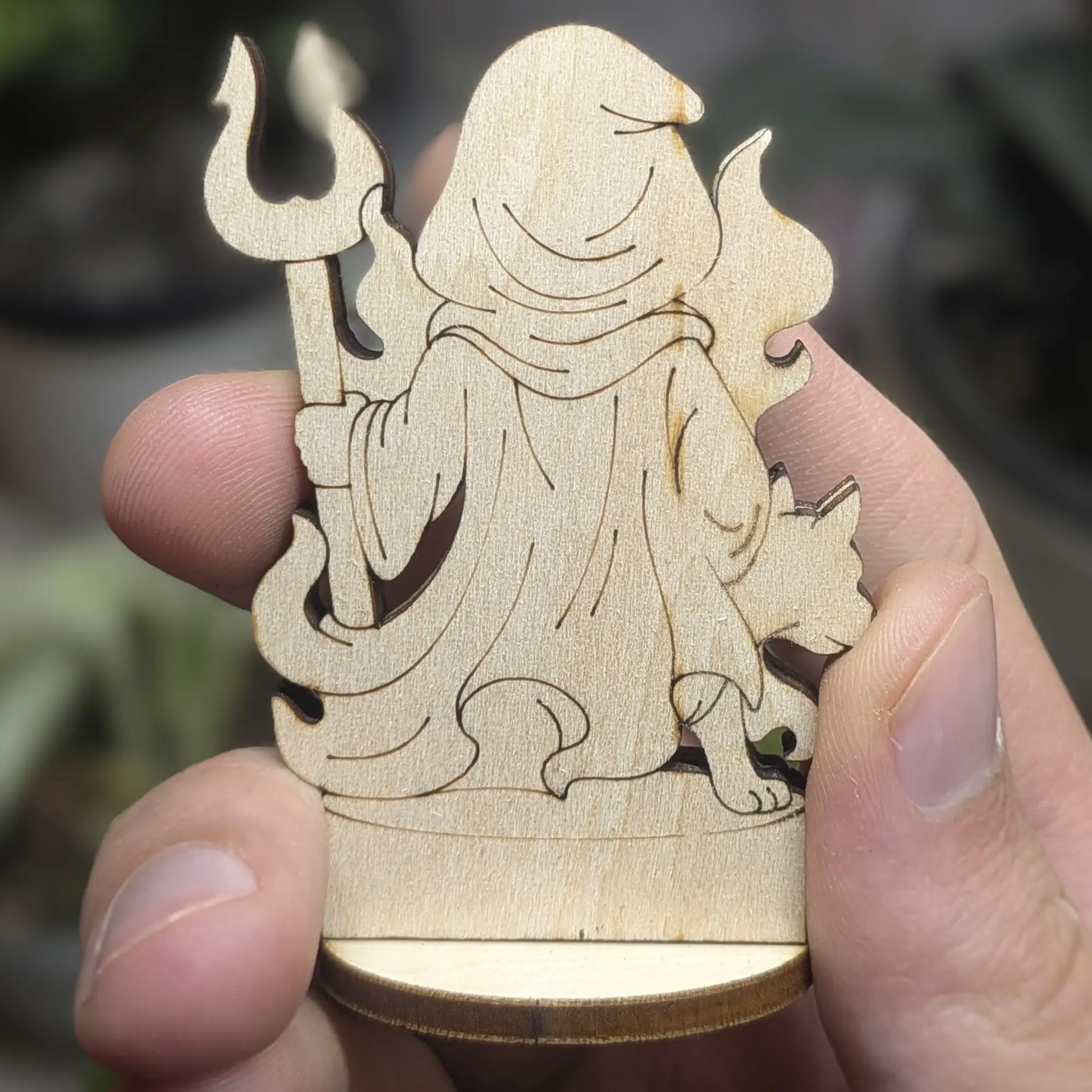 Back view of laser cut plywood Hades held in hand. Shows dark burnt edges, flowing cape, and natural wood grain texture