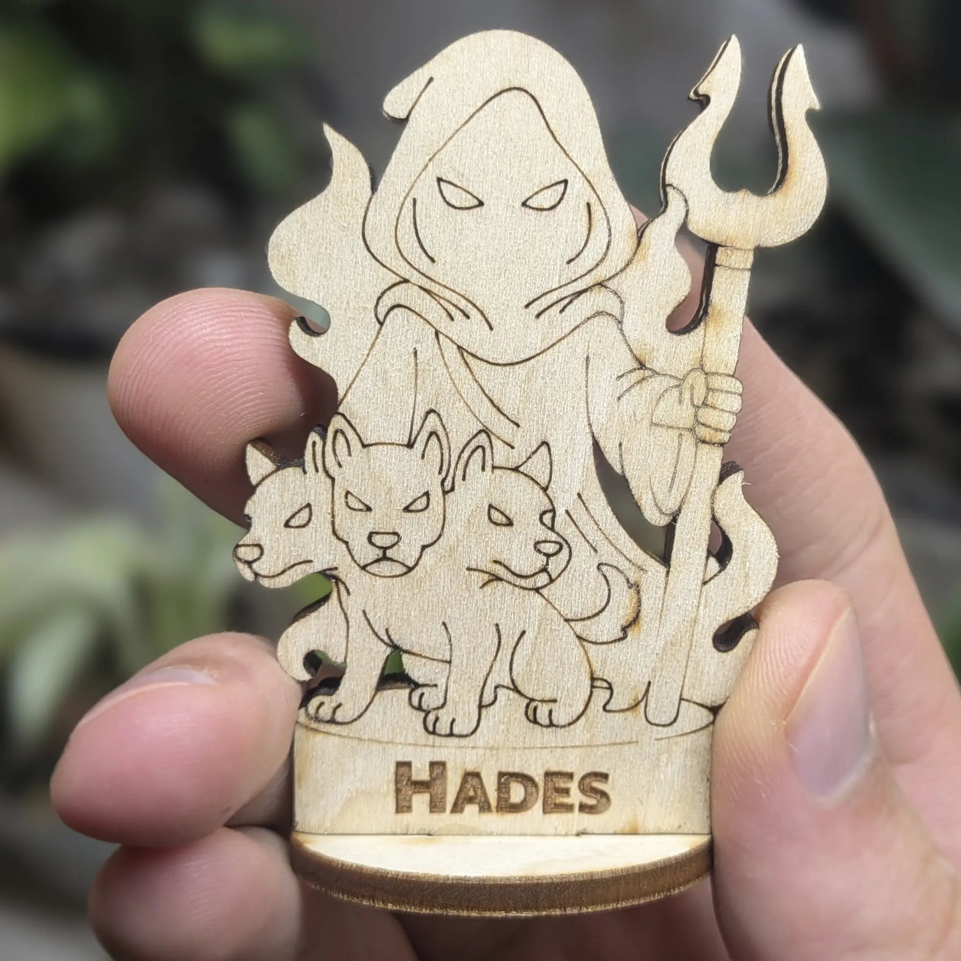 Hand holds a laser cut plywood Hades figurine for scale. Features an engraved crown, bident staff, and detailed robes