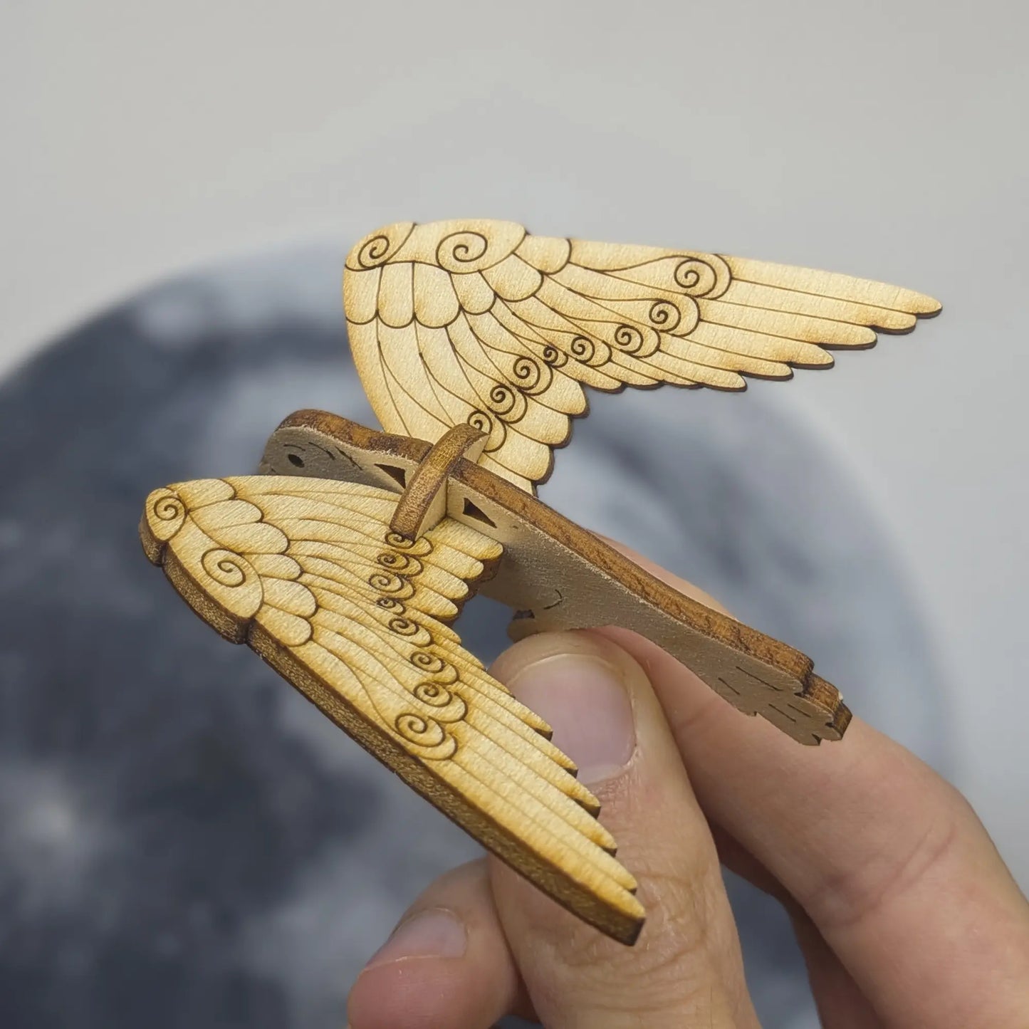Top view of a bird ornament made of laser cut plywood held in hand. Wings feature beautiful engraved spirals and dots