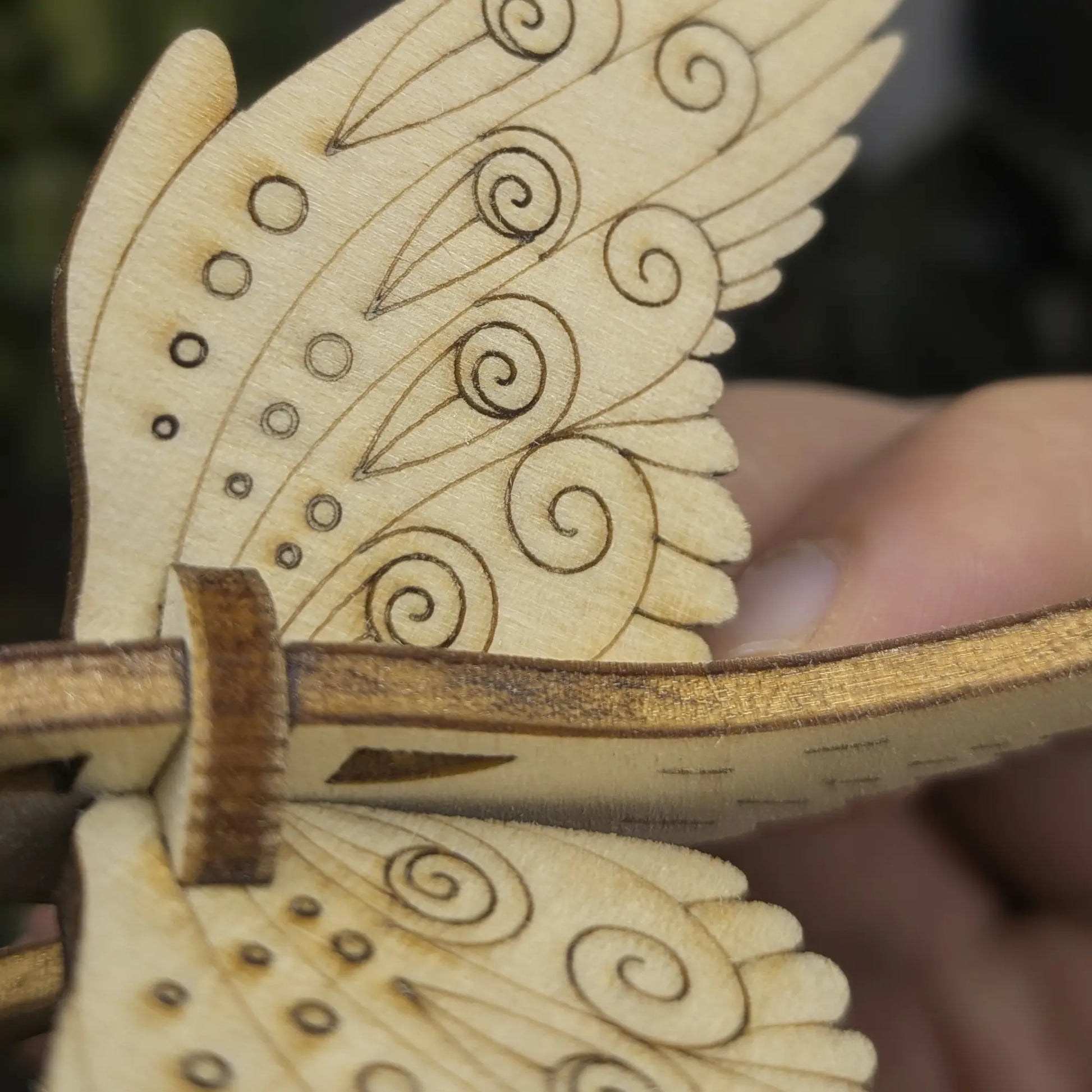 Close-up of wing details on a laser cut plywood bird. Shows precise engraved teardrops, swirls, and decorative dotwork