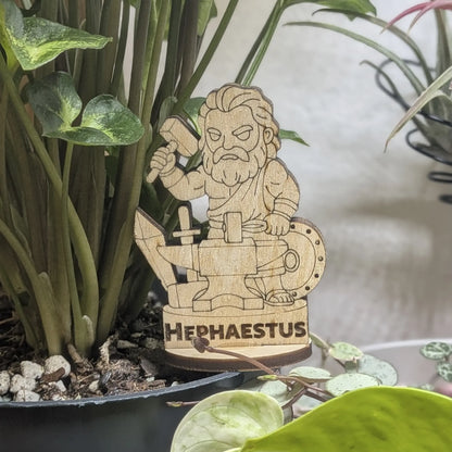 A laser cut plywood Hephaestus figurine in a plant pot. Blacksmith god with a hammer and tongs, featuring fine engraving