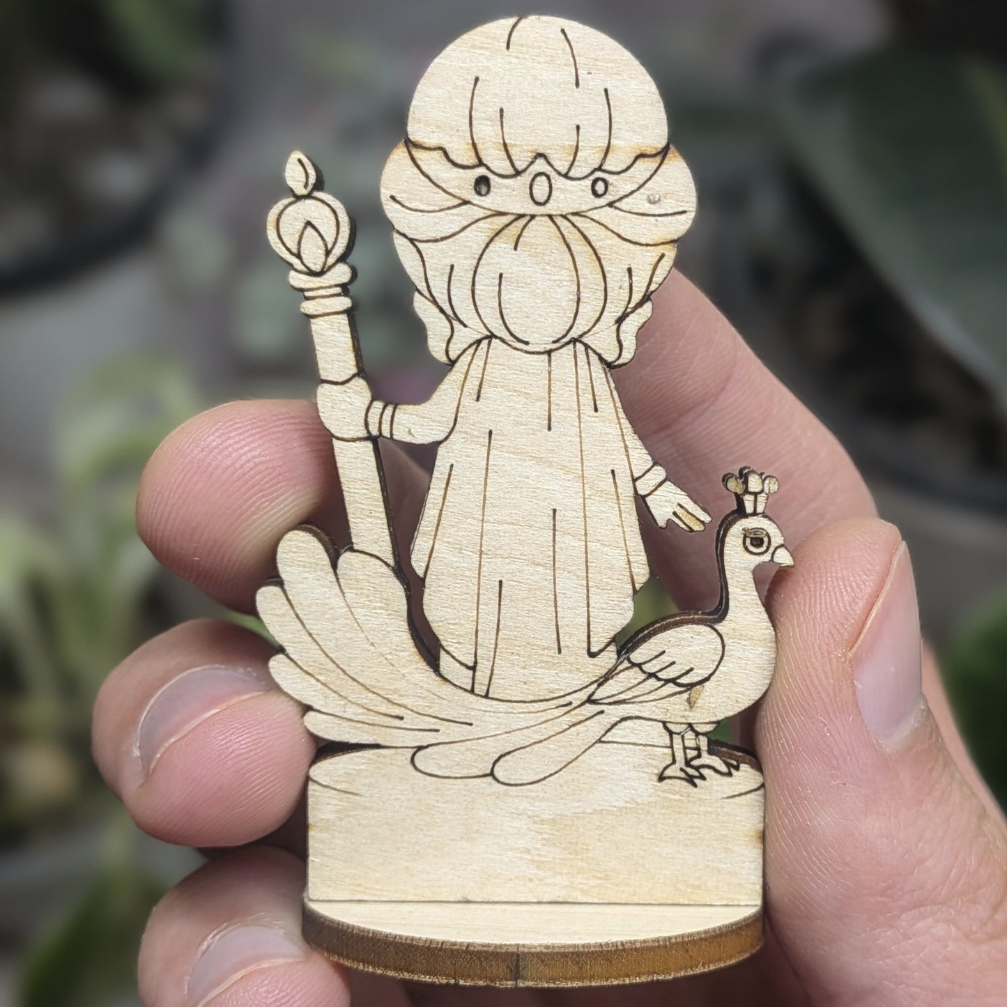 Back view of a laser cut plywood Hera held in hand. Shows dark burnt wood edges, flowing hair, and natural grain texture