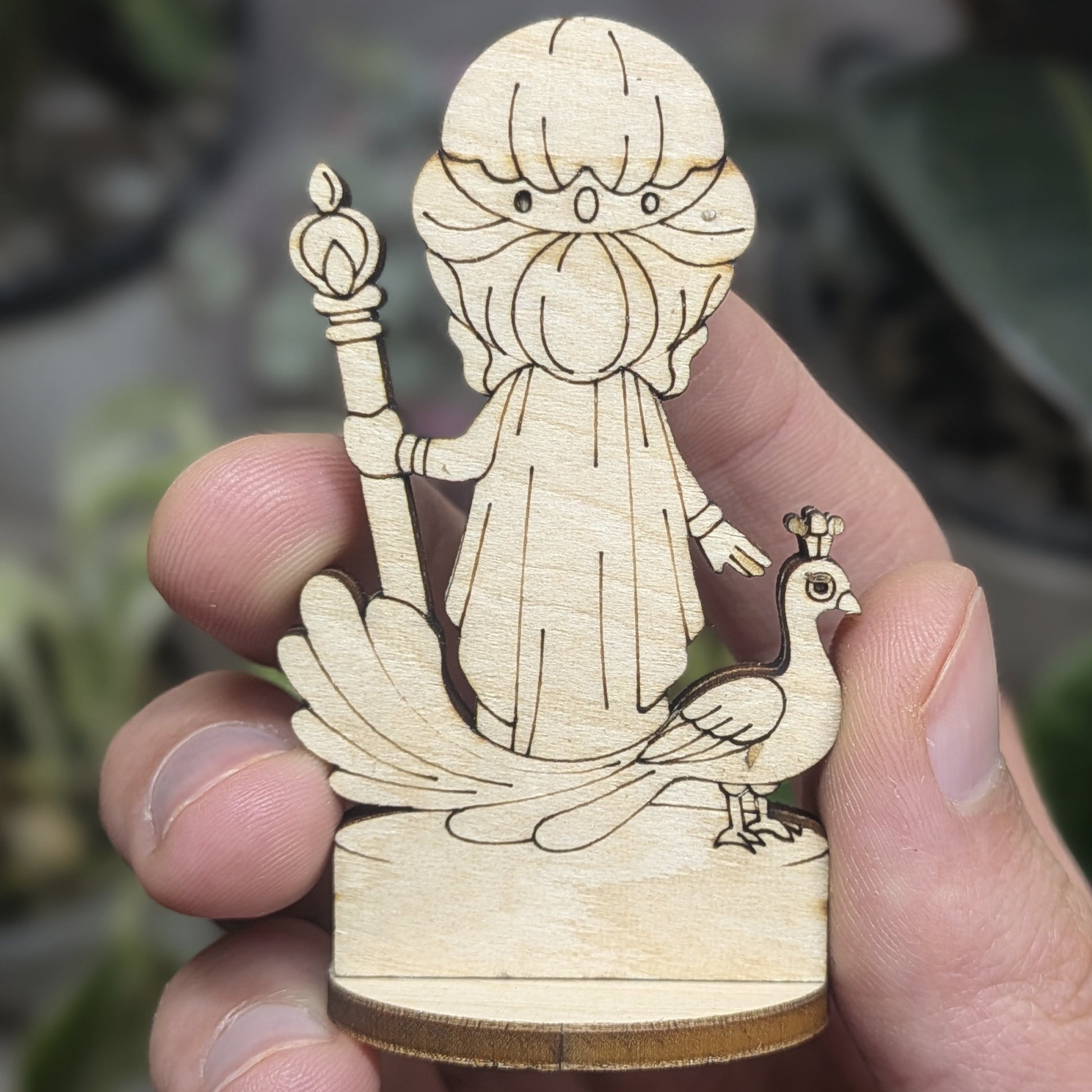 Back view of a laser cut plywood Hera held in hand. Shows dark burnt wood edges, flowing hair, and natural grain texture