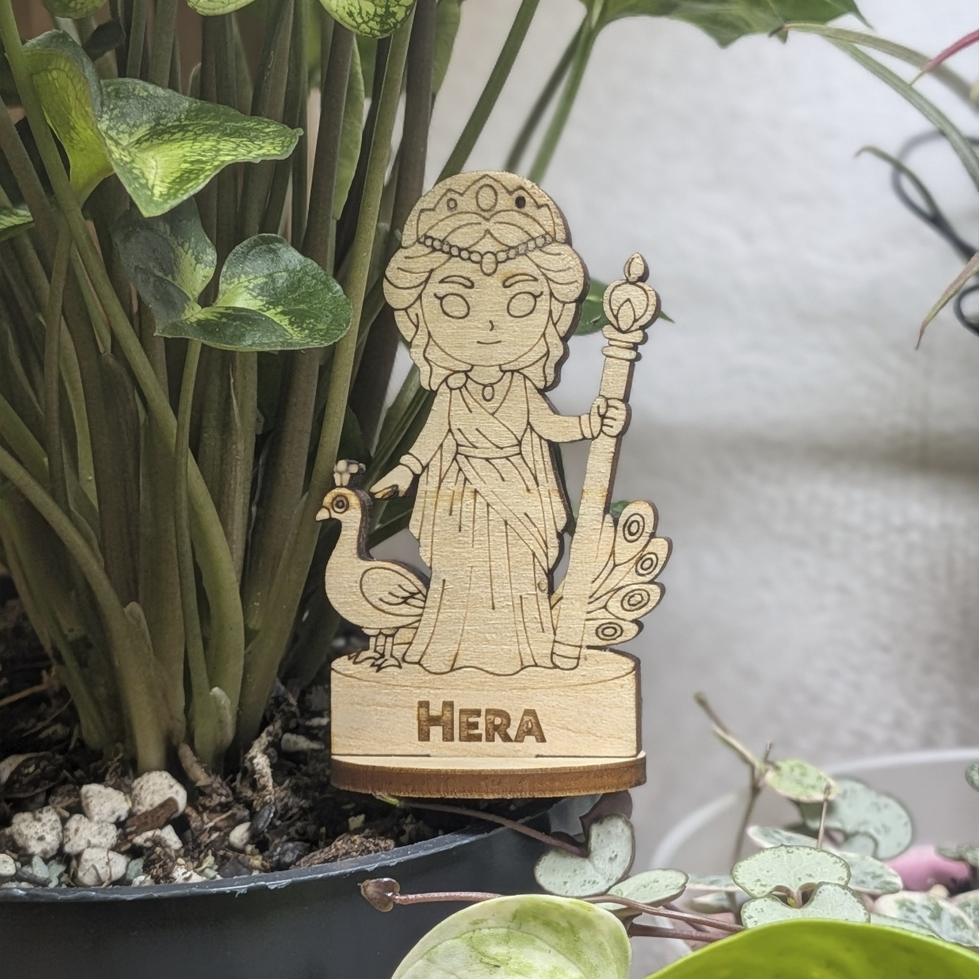 Laser cut plywood Hera figurine staged in a plant pot. Features a royal crown, scepter, and robes on a round wood base