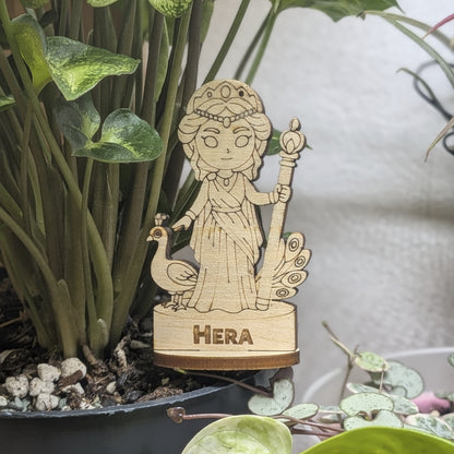 Laser cut plywood Hera figurine staged in a plant pot. Features a royal crown, scepter, and robes on a round wood base
