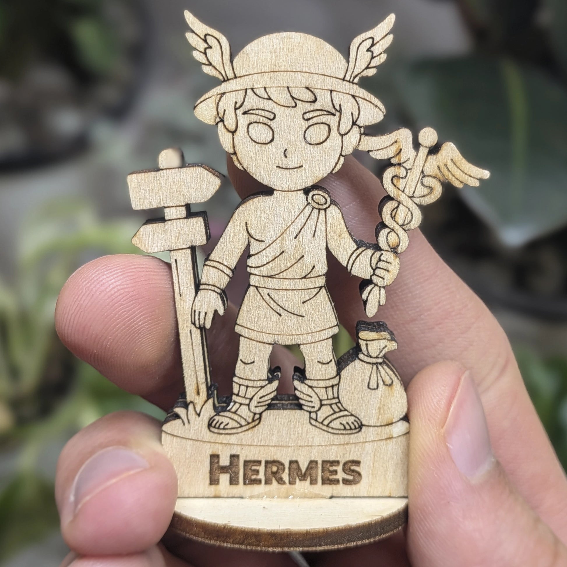 Hand holds a laser cut plywood Hermes for scale. Shows the detailed caduceus, winged hat, and tunic at a miniature scal