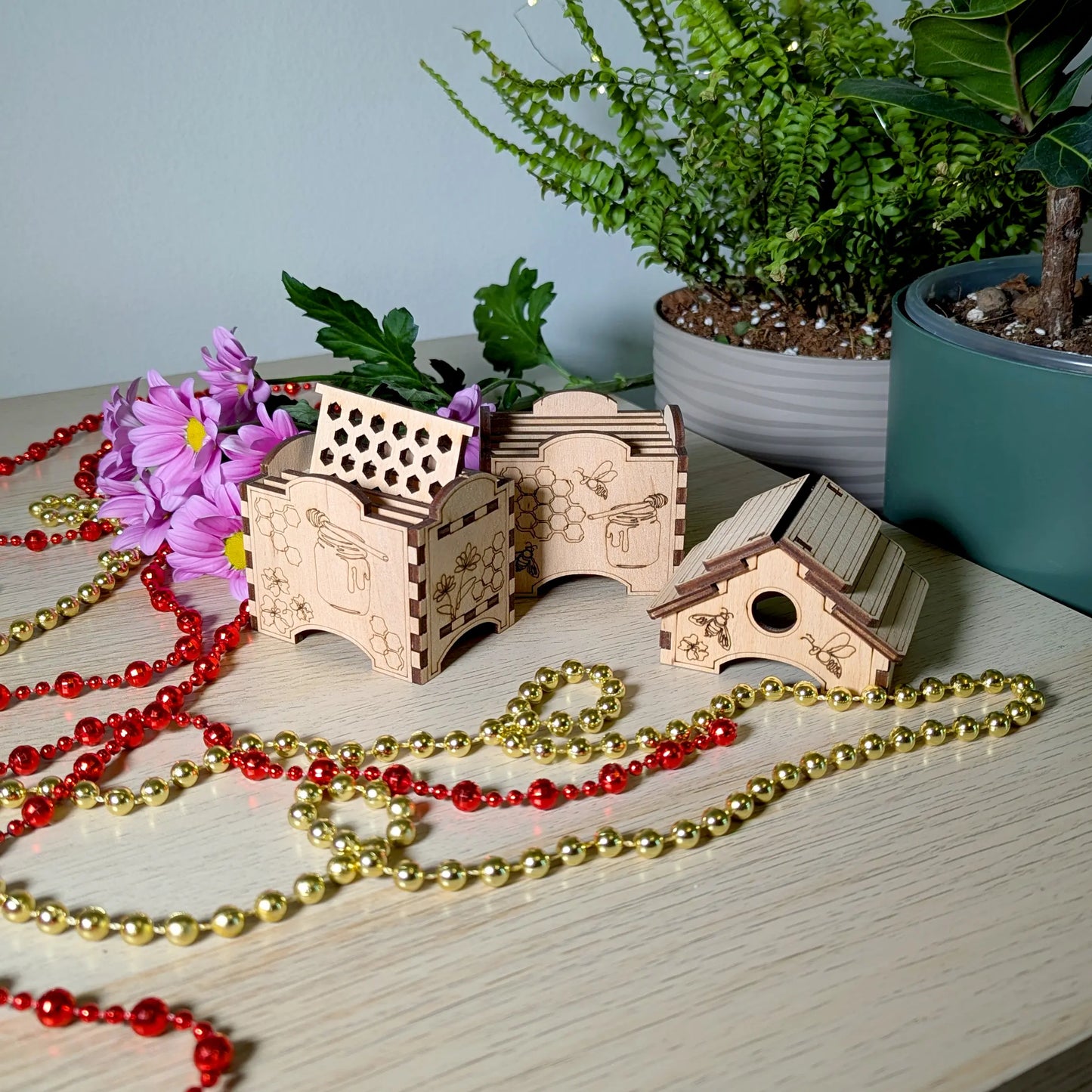 Modular laser cut plywood bee hive boxes and roof piece arranged on a desk with festive beads and fresh flowers.