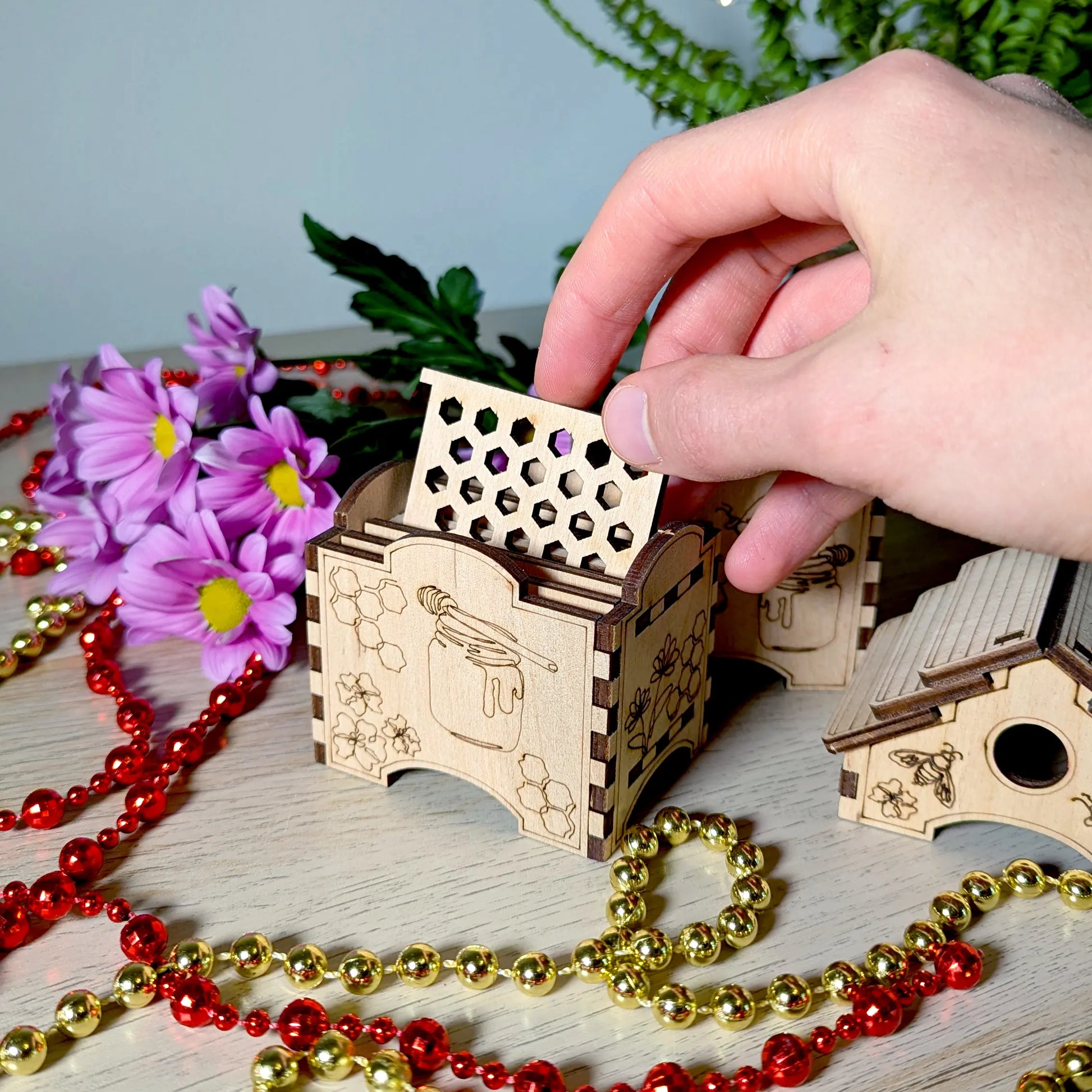 A hand pulling a honeycomb patterned square coaster out of a themed holder made of engraved laser cut plywood.