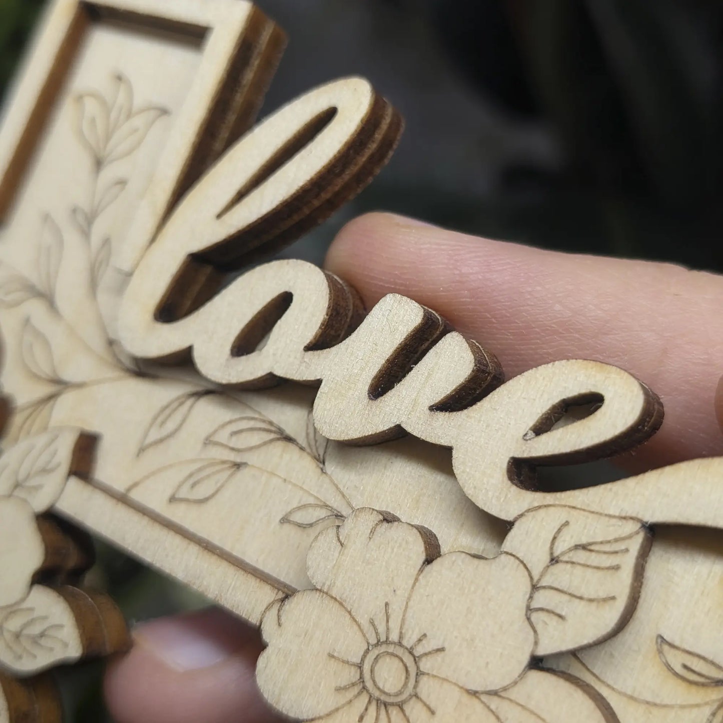 Macro of layered flowers and delicate vine engravings on a laser cut plywood cross. Dark burnt edges highlight wood details