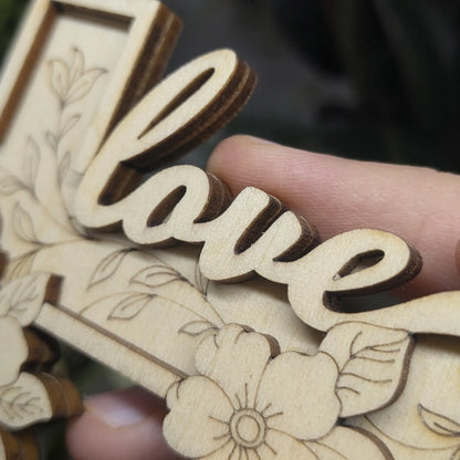 Macro of layered flowers and delicate vine engravings on a laser cut plywood cross. Dark burnt edges highlight wood details