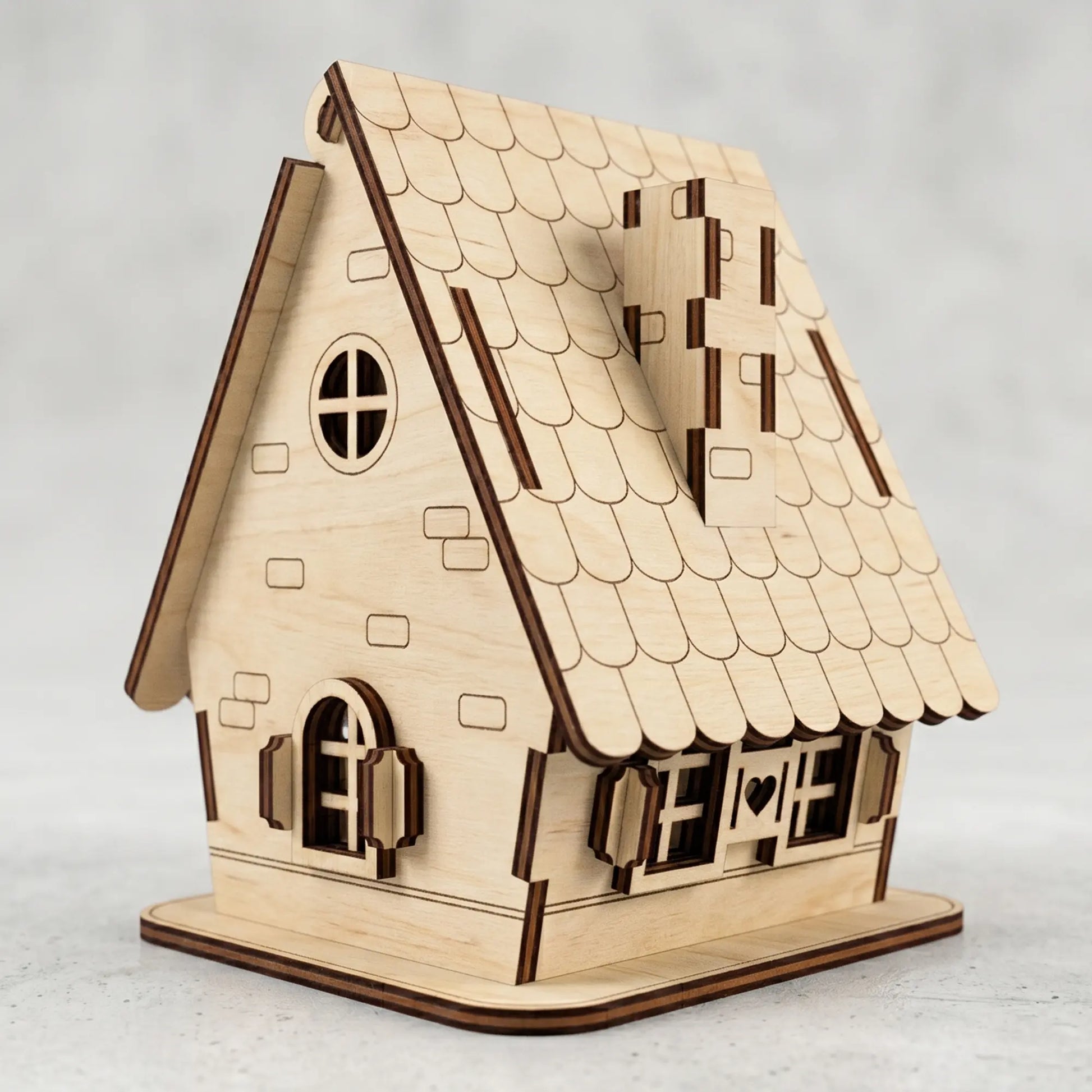 Laser cut plywood miniature house featuring a tiled roof pattern, small shuttered windows, and a side chimney.