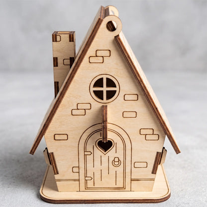 Front view of a laser cut plywood toy house with a chimney, a heart-shaped door detail, and brick engravings.