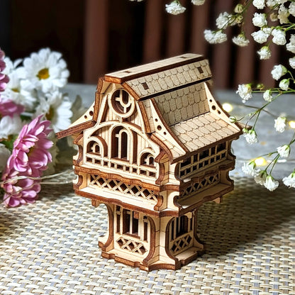 Miniature laser cut plywood cottage standing on a woven mat, beautifully staged with white gypsophila flowers and fairy lights.