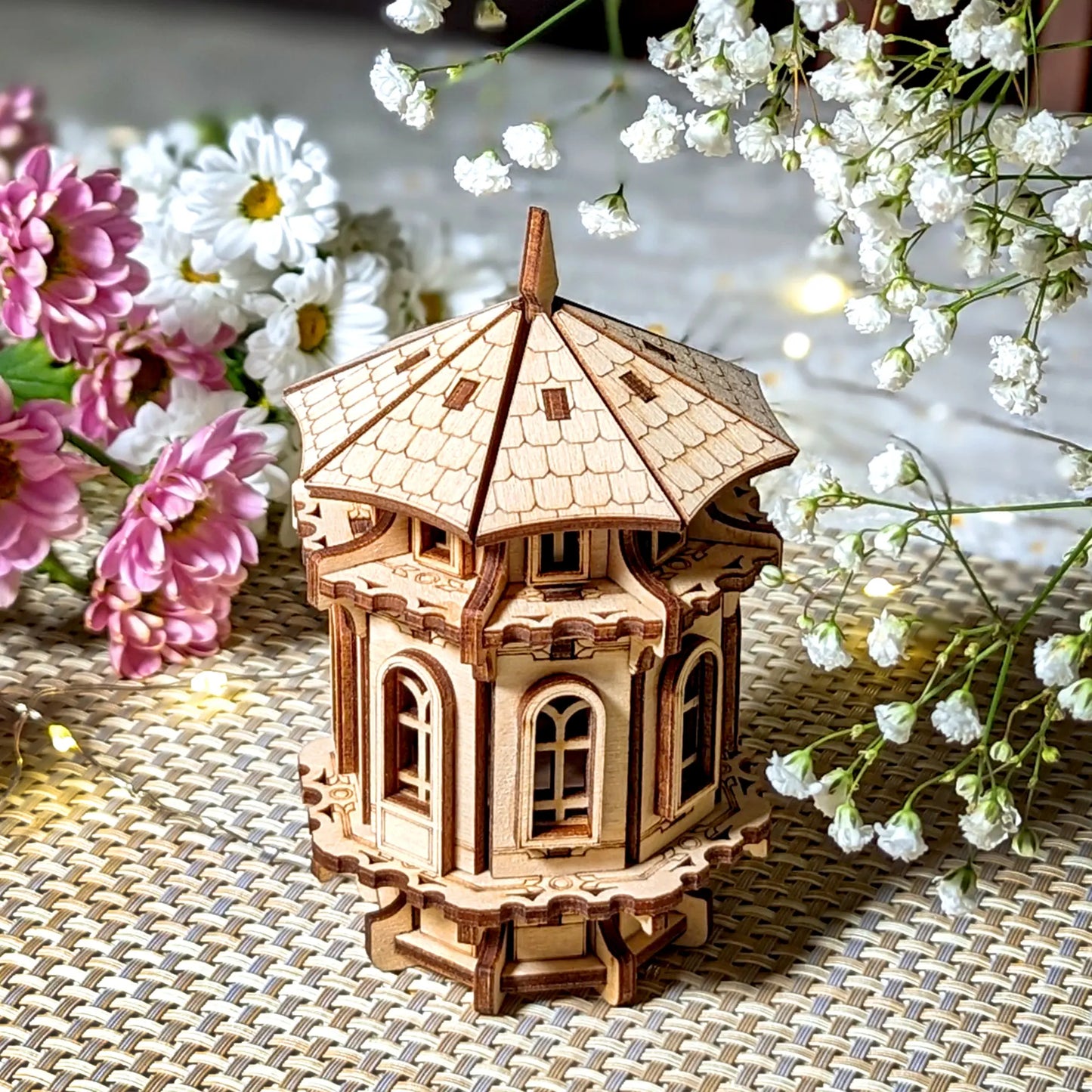 Octagonal tower miniature made of laser cut plywood, staged on a dining table with fresh pink and white daisy blossoms.
