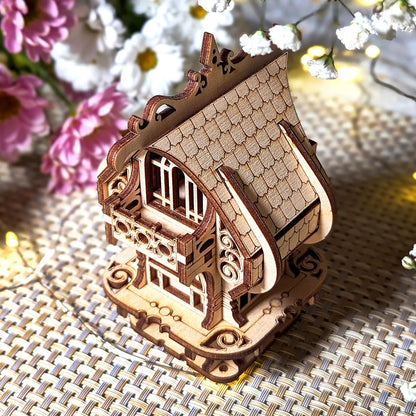 Detailed laser cut plywood miniature fairy house with delicate balcony, arched windows, and tiled roof. Staged with flowers.