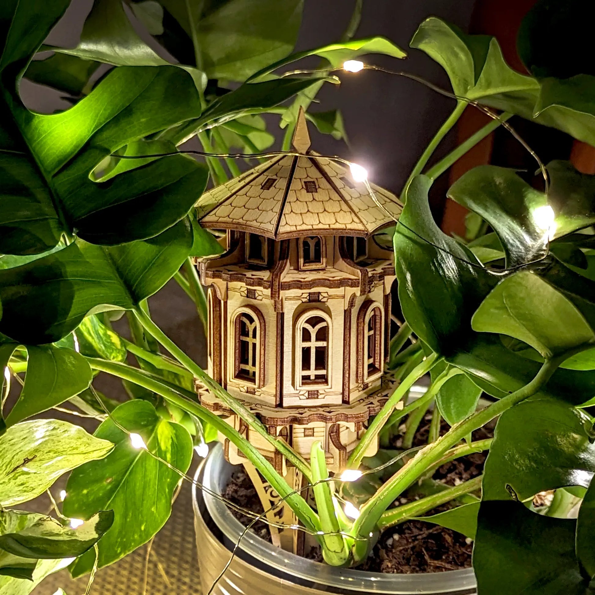 Laser cut plywood garden tower among green leaves, capturing its elegant wood aesthetic and scale.