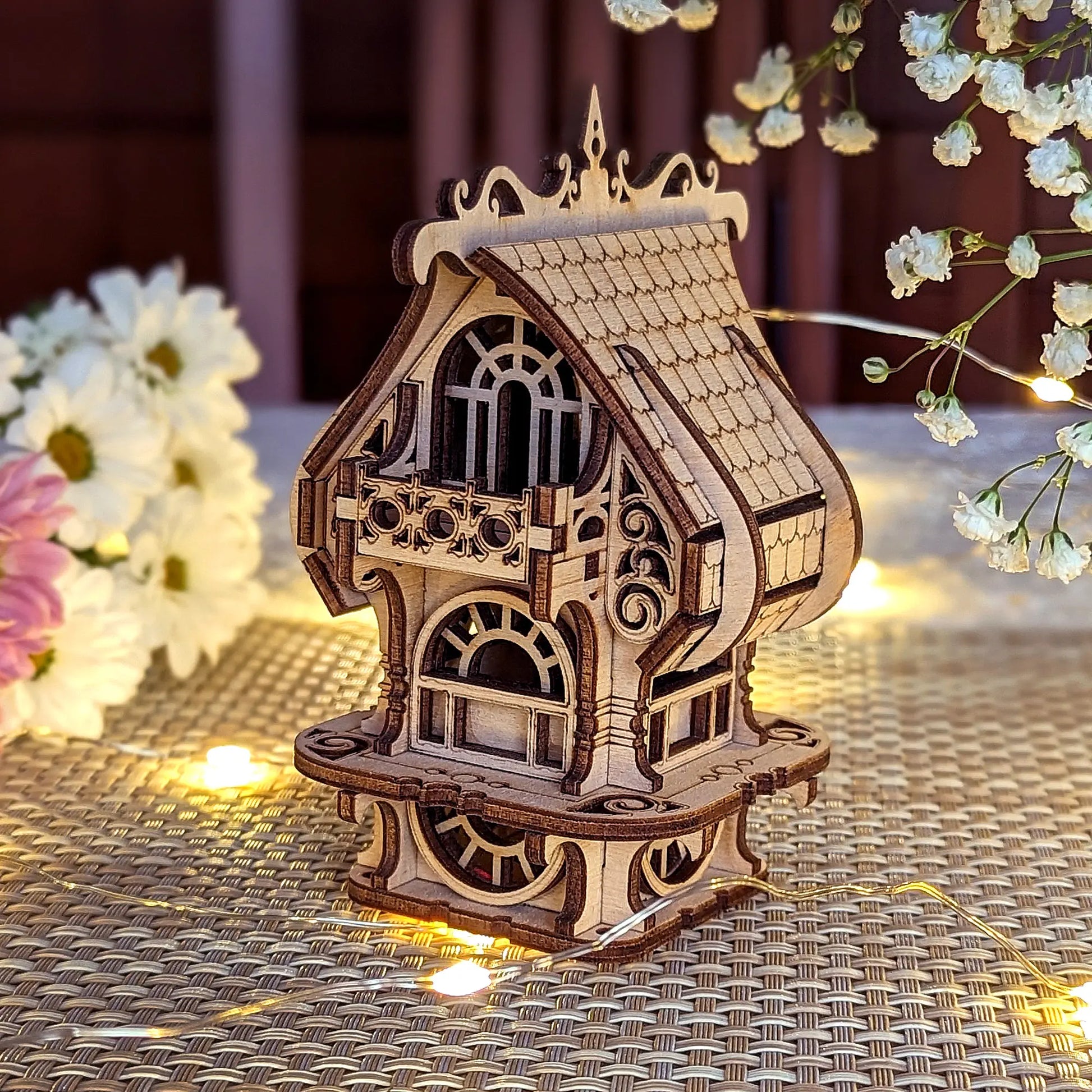Elegant laser cut plywood fairy house model showing precise wooden details, balcony, and roof. Floral background.