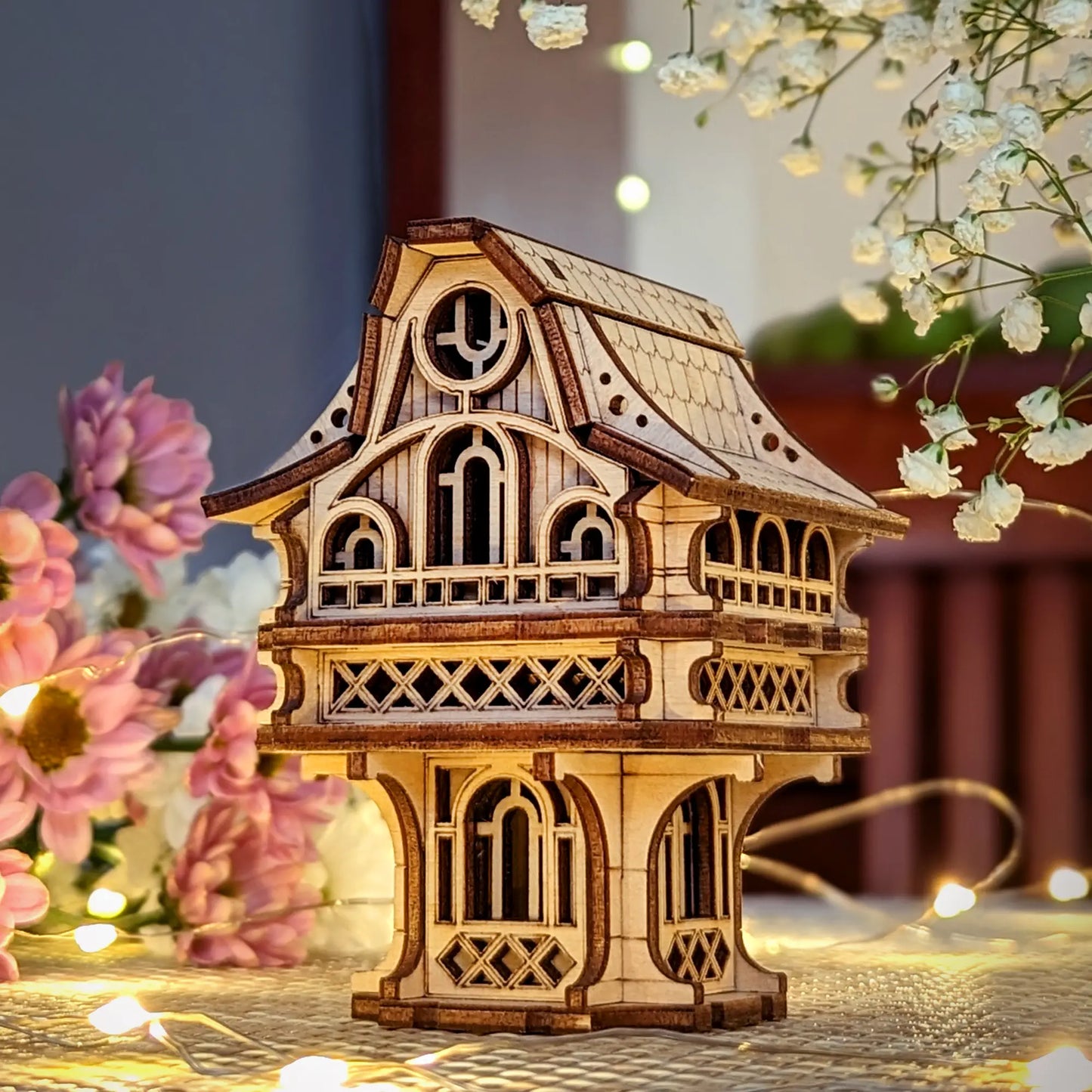 Laser cut plywood gnome house on a table decorated with flowers and fairy lights, showcasing its detailed wooden texture.