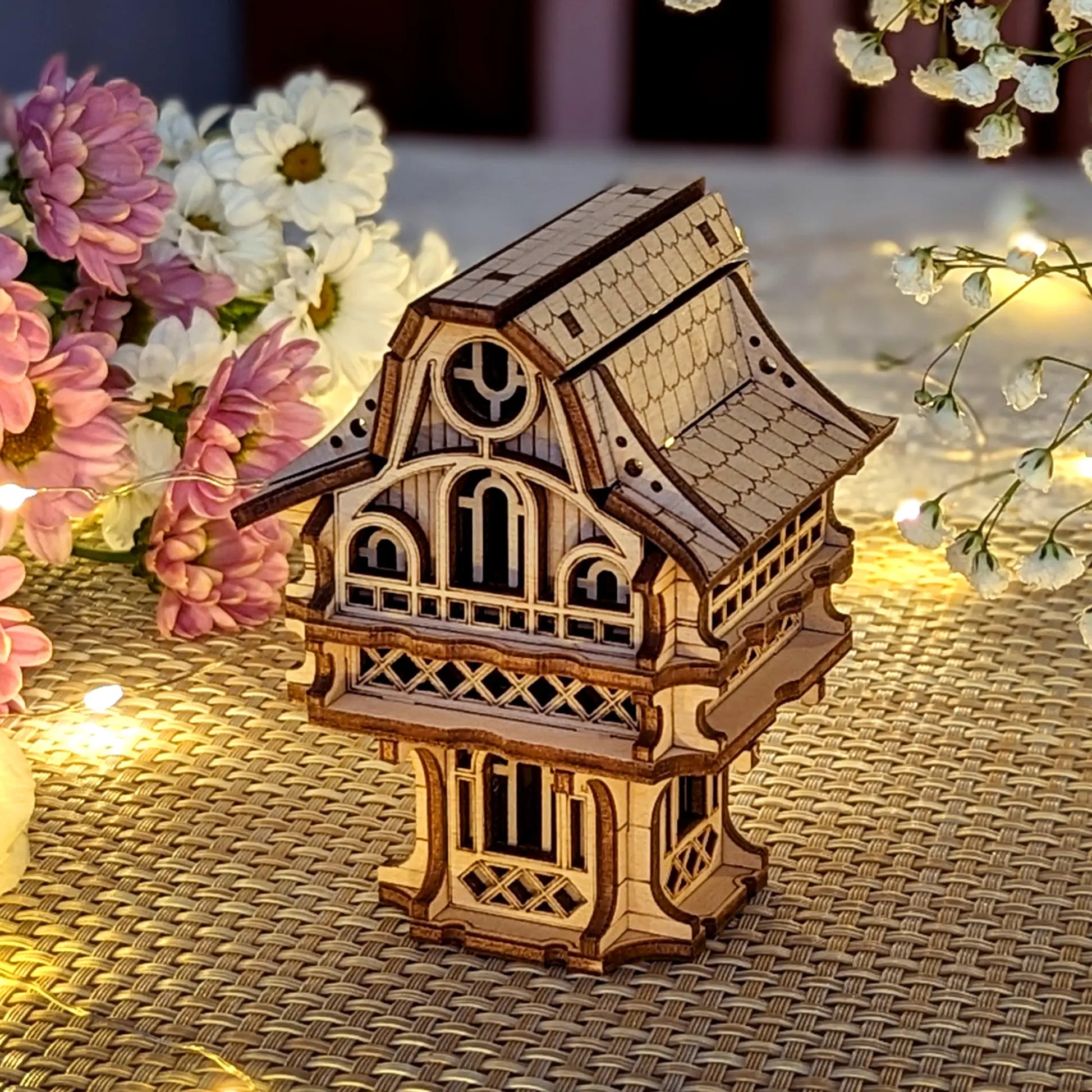 Decorative laser cut plywood gnome house standing on a textured mat, surrounded by soft-focus flowers and warm lighting.