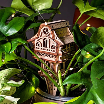 Artistic close-up of a laser cut plywood gnome house placed within lush indoor plants, enhanced by glowing fairy lights.