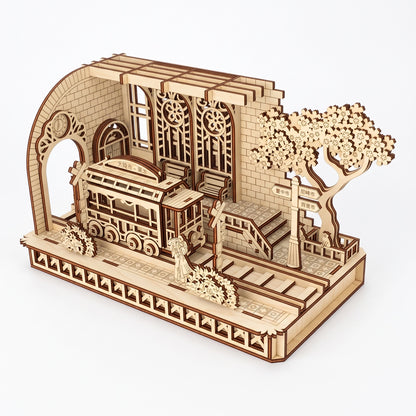 Three-quarter view of a laser-cut birch plywood Japanese tram station featuring a detailed tram, tracks, and a blossoming tree.