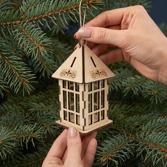 Hands hold laser cut plywood pagoda lantern ornament with lattice sides showing scale by pine branches