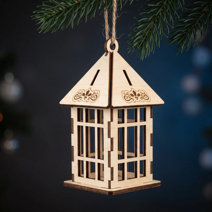 Hanging laser cut plywood holiday lantern ornament with engraved holly motif against deep blue pine backdrop