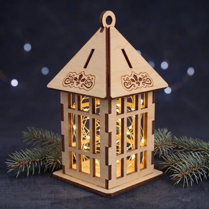 Laser cut plywood lantern illuminated from inside with fairy lights, resting on dark fabric with pine sprigs