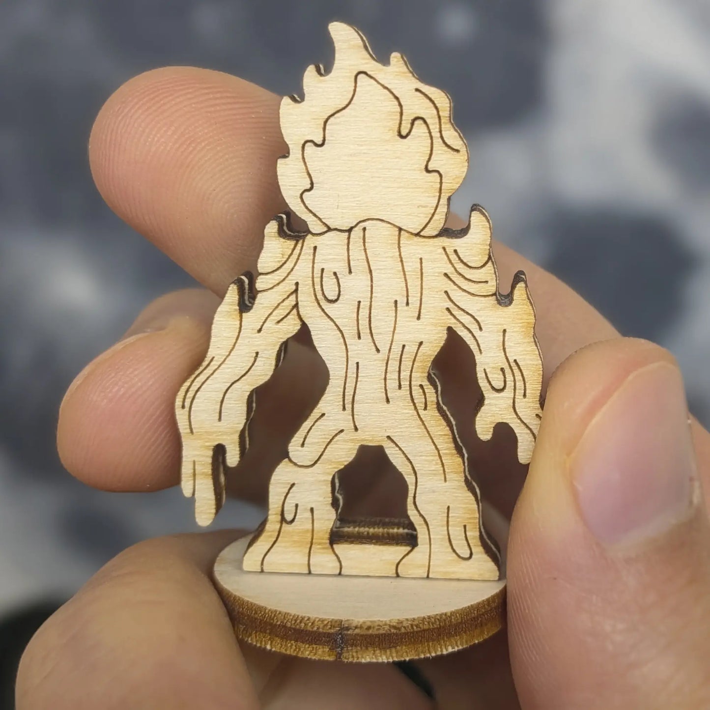 Back view of a laser cut plywood lava elemental figurine held by hand. Shows vertical wood grain and dripping magma drips