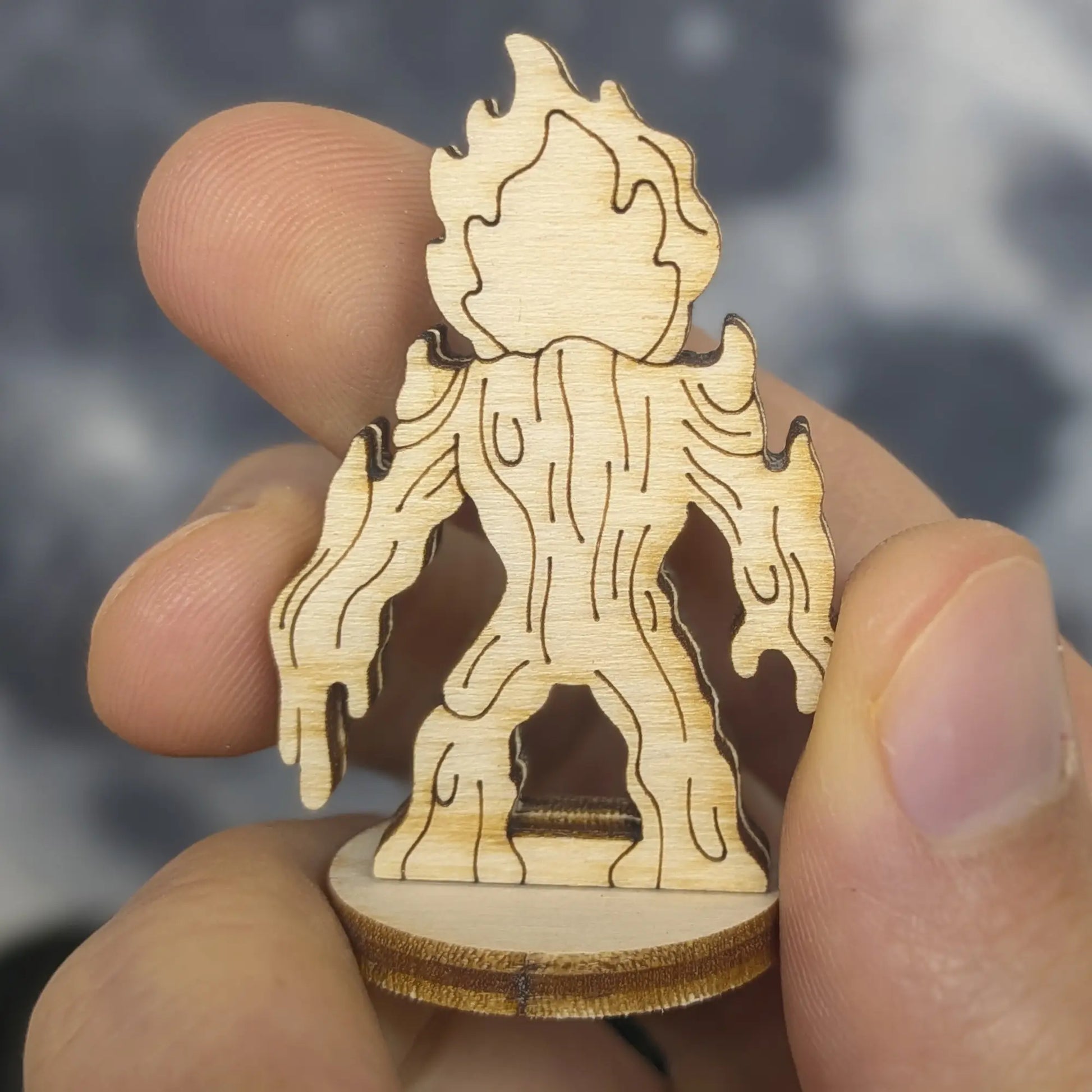 Back view of a laser cut plywood lava elemental figurine held by hand. Shows vertical wood grain and dripping magma drips