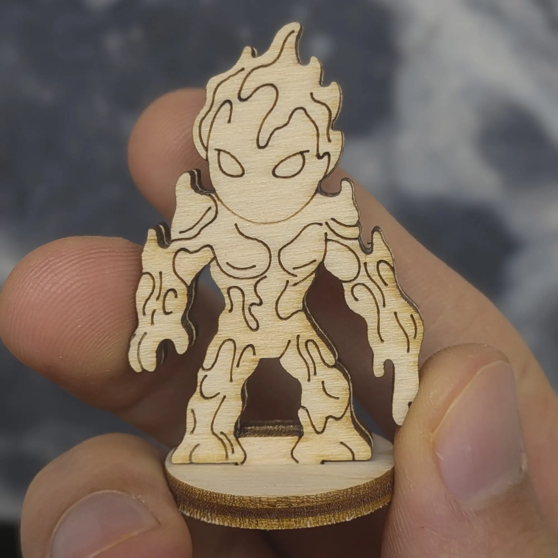 Hand holds a laser cut plywood lava elemental figurine. Front view shows engraved dripping magma, blank eyes, and fire head