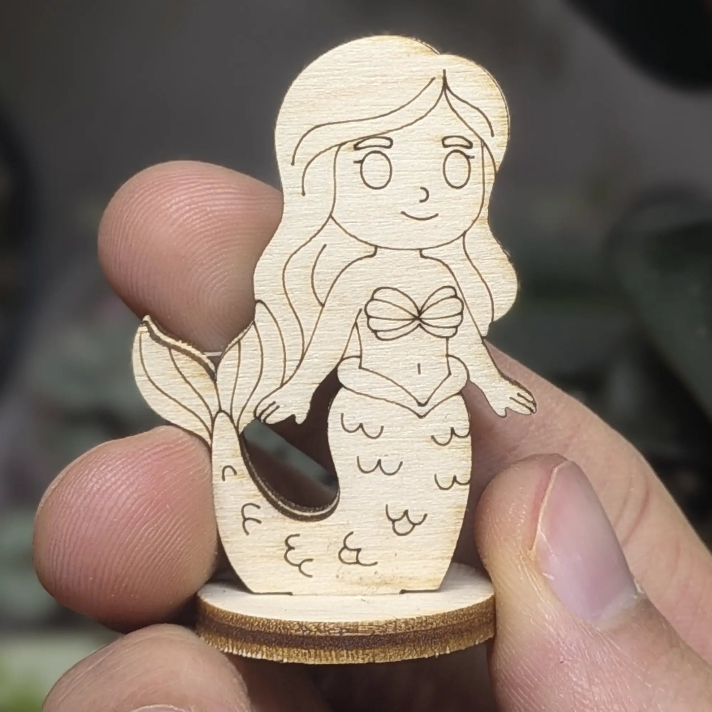 Hand holds a laser cut plywood mermaid figurine for scale. Features detailed engraved scales, shell top, and flowing hair