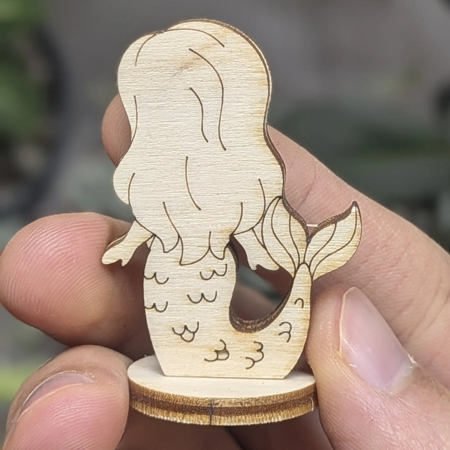 Back of laser cut plywood mermaid held in hand. Highlights flowing hair texture, tail fin detail, and smooth wood finish