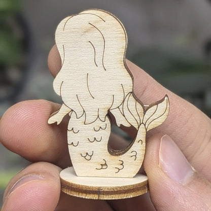 Back of laser cut plywood mermaid held in hand. Highlights flowing hair texture, tail fin detail, and smooth wood finish