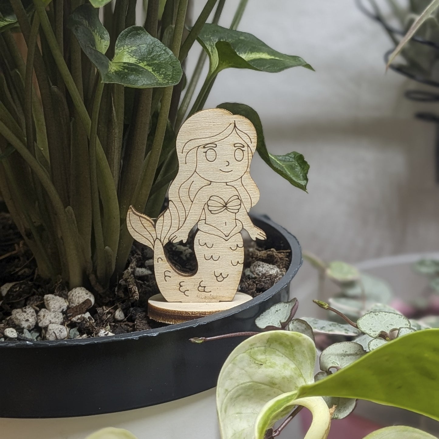 Laser cut plywood mermaid toy standing in a green plant pot. Detailed shell top, long hair, and scales engraved on wood